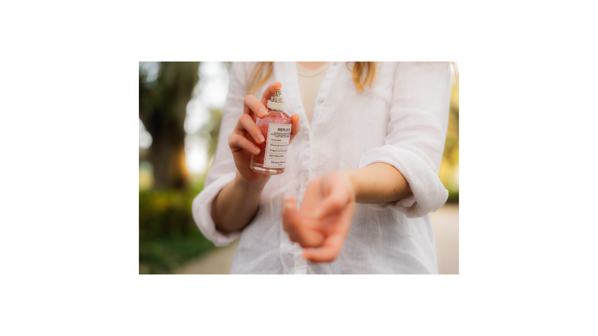 On-set — model in white linen spraying the REPLICA bottle, late-afternoon outdoor light