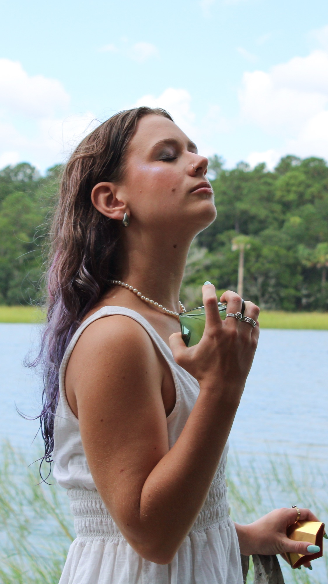 Salted Muse editorial — the model lakeside in white linen, the bottle to her throat, head tipped to the sky